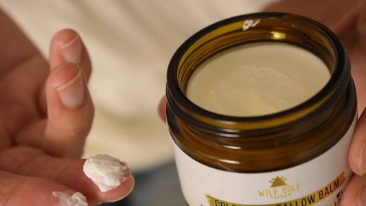 Tallow balm under makeup: pale ivory whipped balm on a fingertip beside an open jar of Wild Gold Tallow