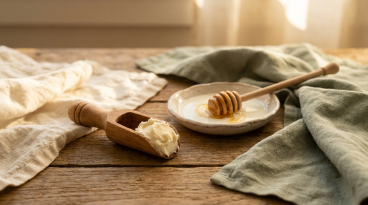 Colostrum face cream ingredients: soft cream-colored balm on a wooden scoop beside raw milk and honey on natural wood